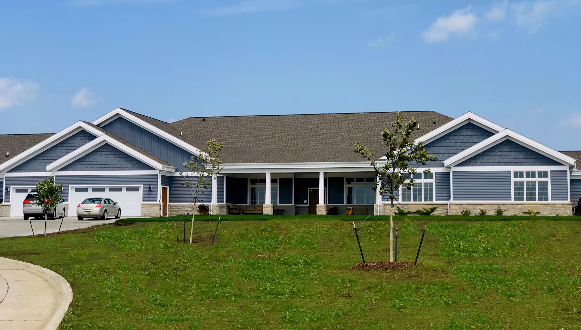 Front exterior of a single-story blue-sided building with attached garages, a covered entrance, and a grassy lawn.