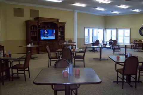Interior senior living dining area with scattered tables, chairs, and a large TV cabinet.