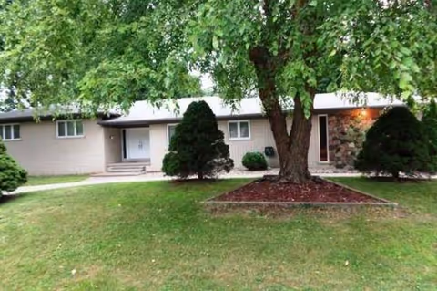 Single-story senior living building with a lawn, trees, and a front entrance.
