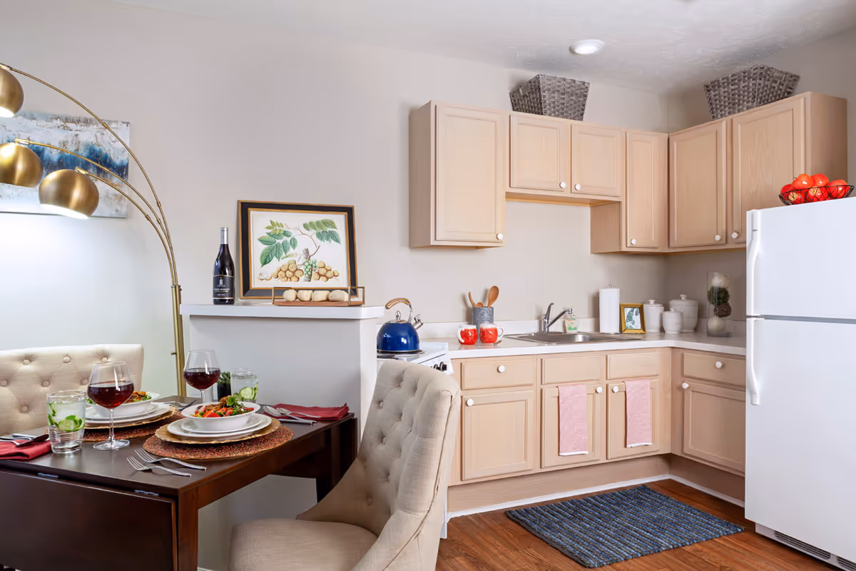 Small kitchen and dining nook with light wood cabinets, a white refrigerator, and a set table with tufted chairs.