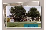Exterior view of Pleasant View Home, a single-story building with a white exterior and multiple windows, surrounded by green grass and large trees. A sign in front reads 'Pleasant View Home'.