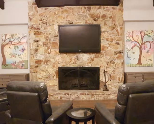 Cozy living room with a stone fireplace, wall-mounted TV, two leather recliners, and a small round table.