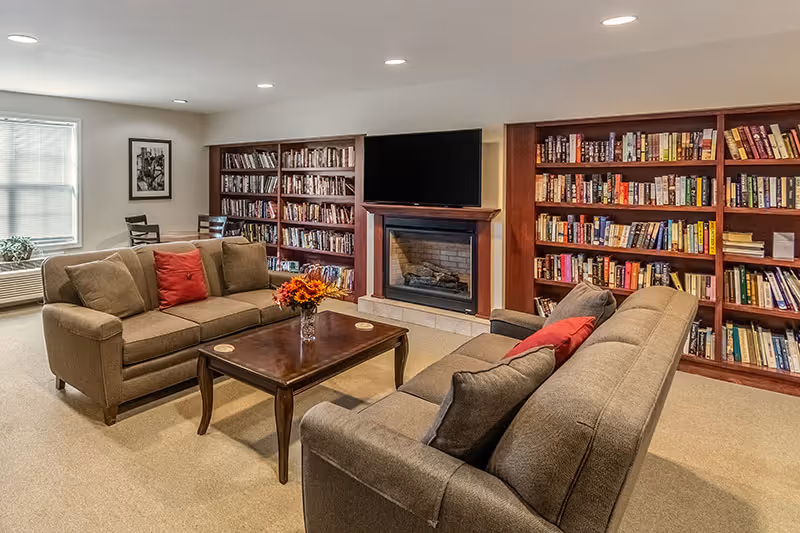 Cozy common living room with sofas around a coffee table, a fireplace and TV, and bookshelves lining the walls.