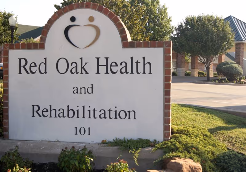 Outdoor view of a large sign for Red Oak Health and Rehabilitation Center with landscaping and part of the building visible in the background.