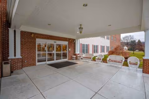 Covered entrance patio of a brick senior living facility with glass doors and seating.