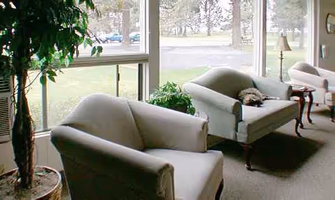 Bright interior lounge with light chairs, a sofa, plants, and large windows.