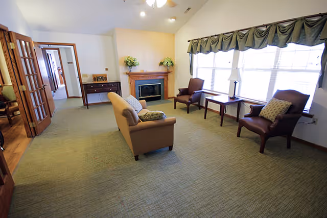 Spacious common living room with a sofa, two armchairs, a fireplace and large windows with valances.