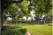 Green lawn with trees in front of a low building, sign reads The Guest House.
