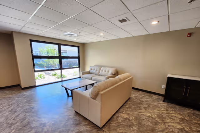 A small sitting area with two beige sofas, a coffee table, and a large window overlooking landscaped grounds.