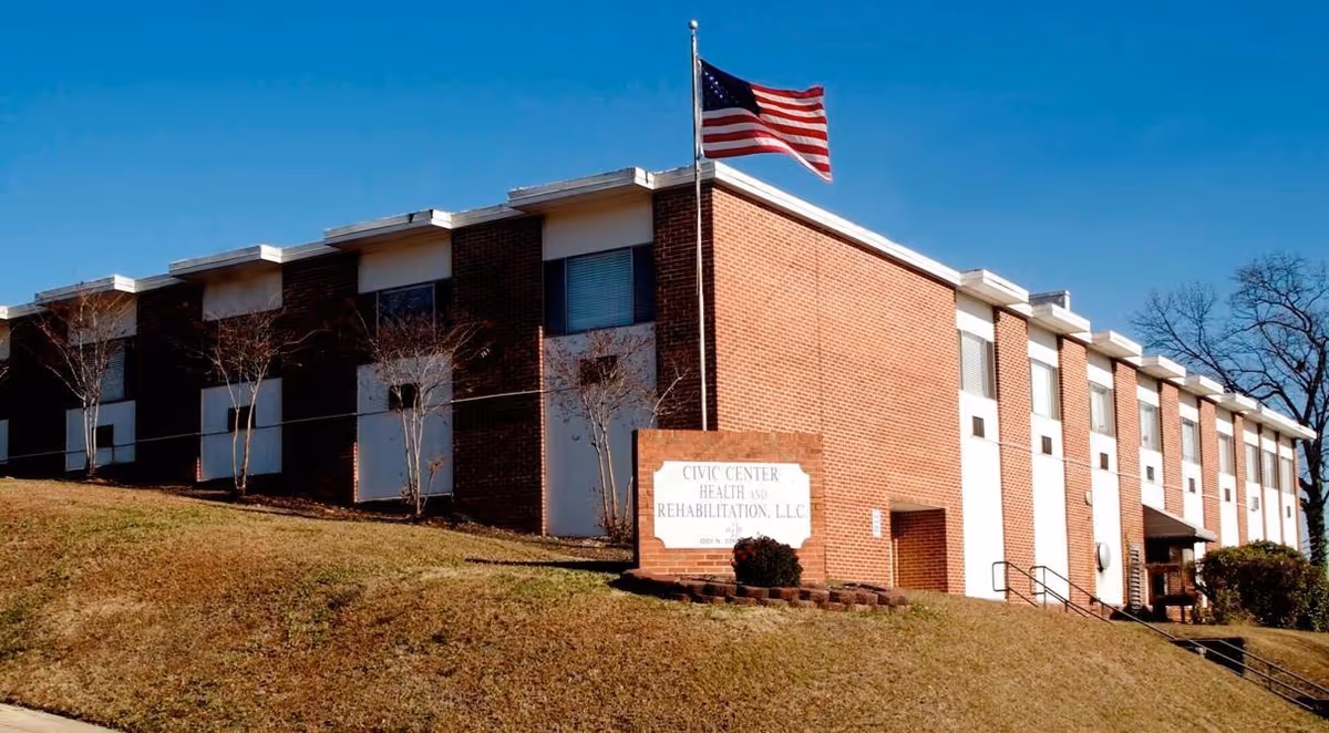 Exterior view of a two-story brick building with multiple windows, an American flag on a flagpole, and a sign that reads 'Civic Center Health and Rehabilitation, LLC' on a grassy slope under a clear blue sky.