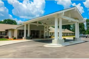 Front exterior of a one-story senior living facility with a covered porte-cochere entrance and paved driveway under a blue sky.