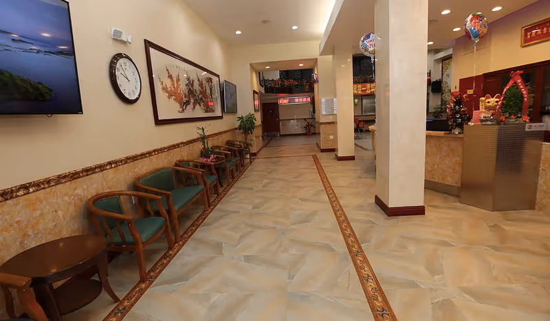 A clean assisted-living lobby corridor with chairs along the left wall, a clock and artwork, tiled floor, and a reception desk on the right.
