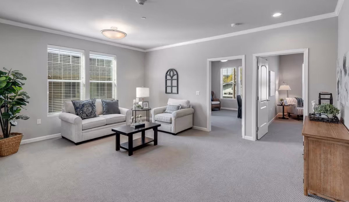 Bright neutral living room with two sofas, a coffee table, a potted plant, and doorways to adjacent rooms.