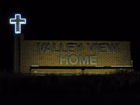 Night view of Valley View Home sign on brick exterior with neon cross.