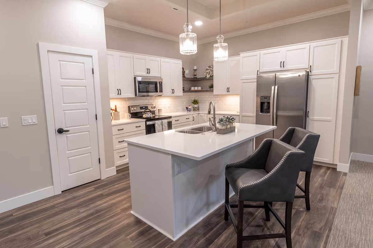 Bright modern kitchen with a central island, two bar stools, white cabinets, stainless steel appliances and pendant lights.