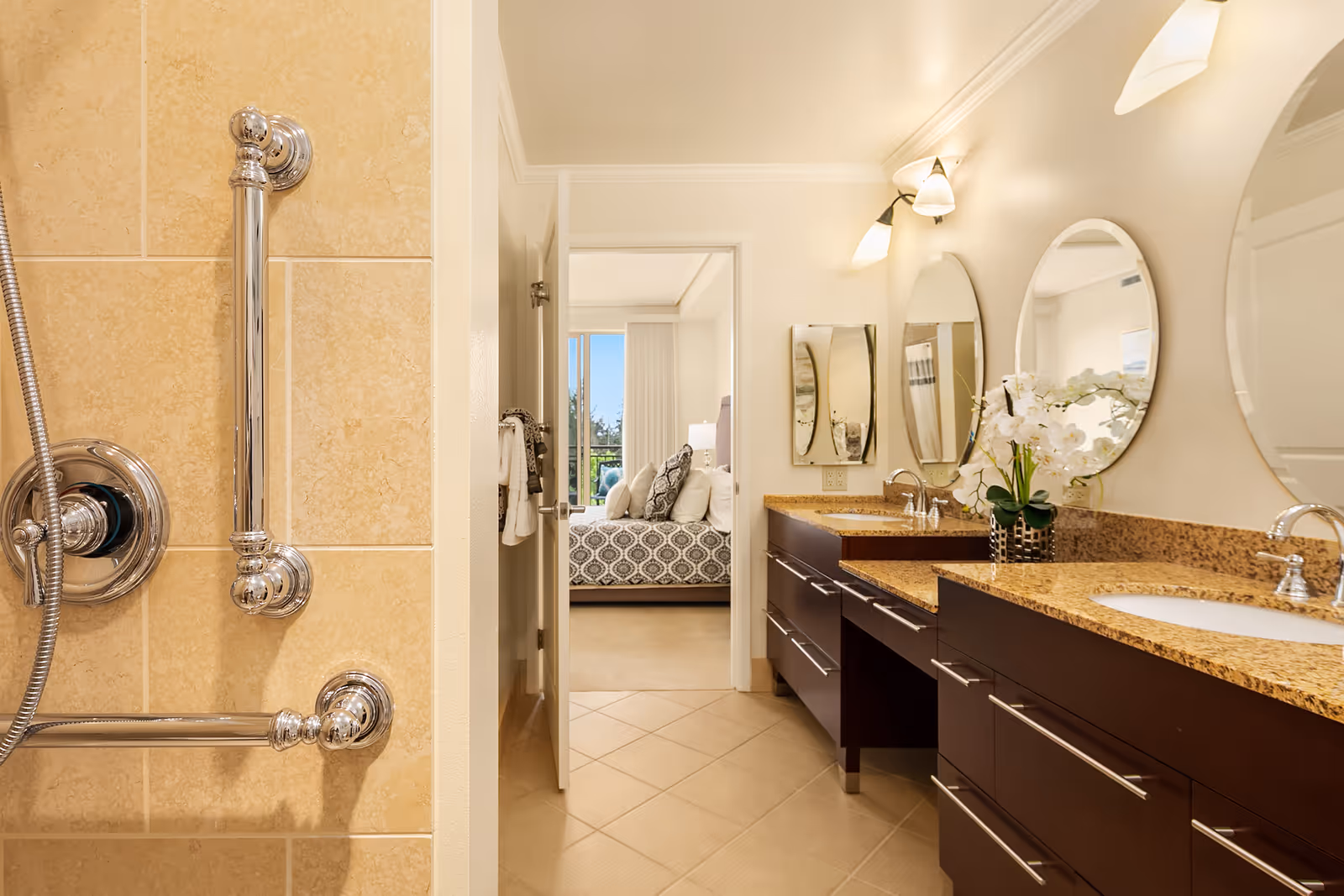 Bright bathroom with double-sink granite vanity, round mirrors, and a view through an open door into a bedroom.