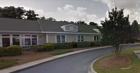 Exterior of a single-story senior living facility with curved driveway and landscaped shrubs.