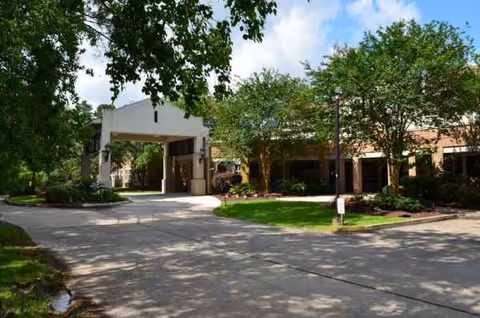 The Grand Cove senior living facility exterior entrance with driveway, trees, and landscaped grounds.