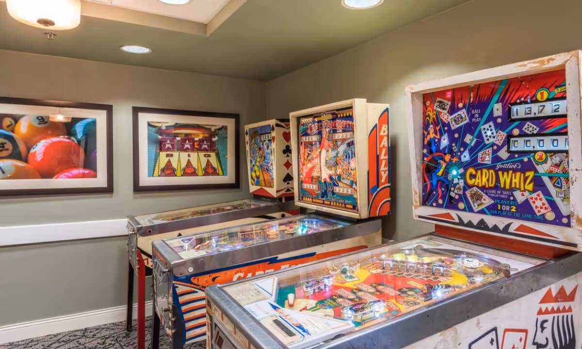 Room interior featuring several vintage pinball machines and framed game-themed artwork on the walls.