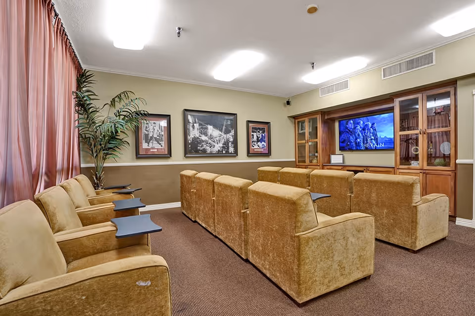Small theater-style media room with rows of upholstered armchairs facing a wall-mounted TV and wooden cabinets.