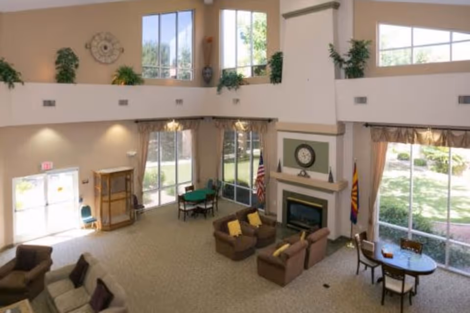 Spacious two-story community lounge with sofas and armchairs around a fireplace, large windows, and tables.
