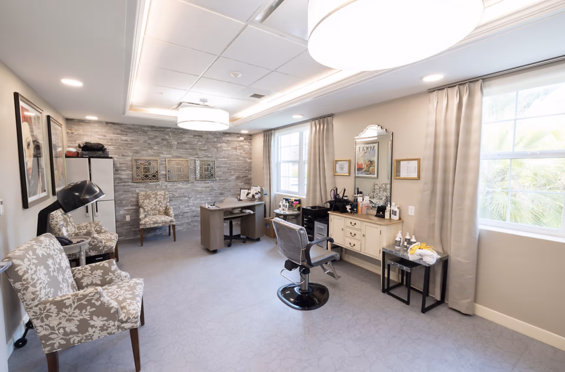 Bright salon-style interior with a styling chair, vanity, patterned armchairs and a decorative stone accent wall.