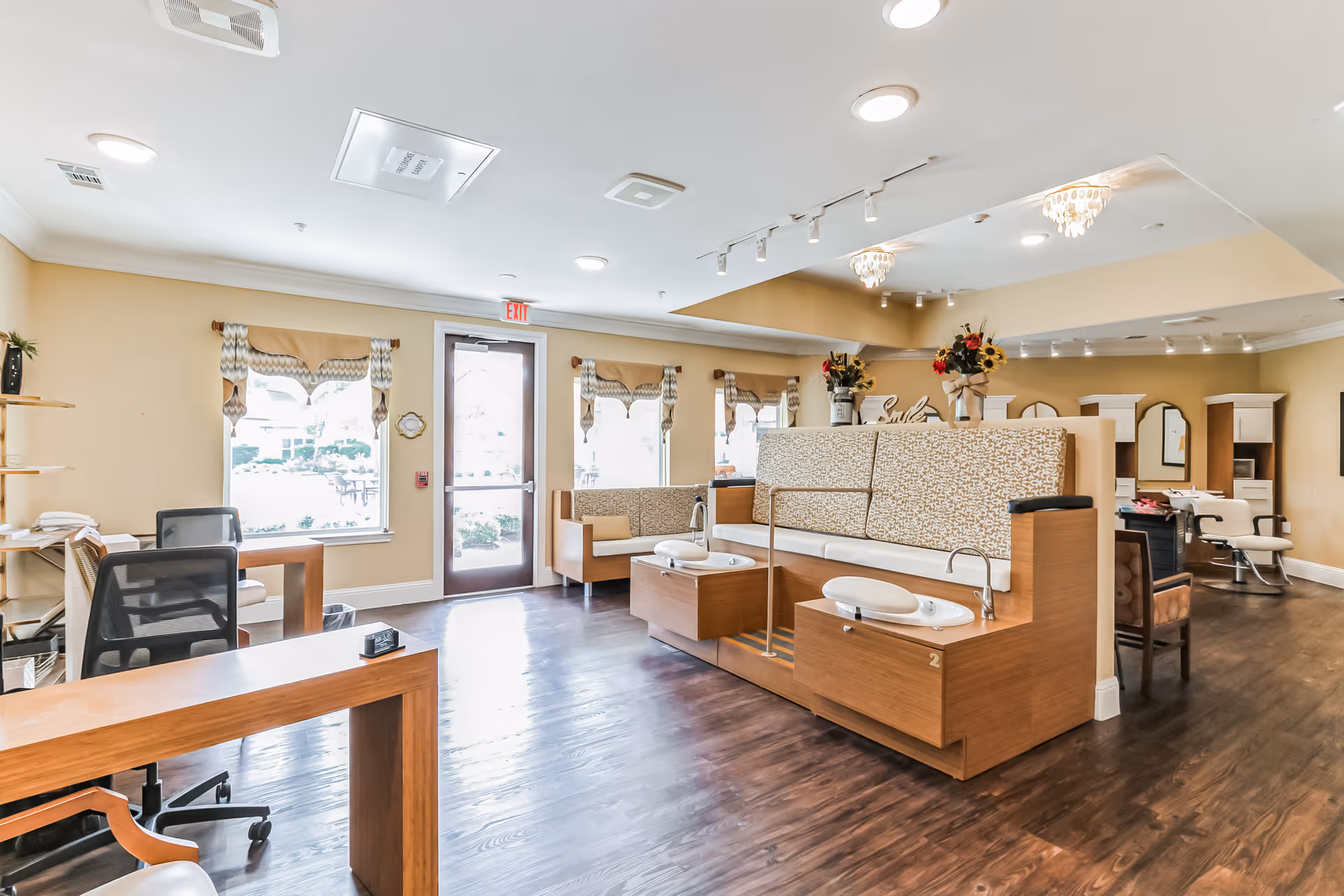 Bright salon-style common room with pedicure stations, seating, desks, and large windows.