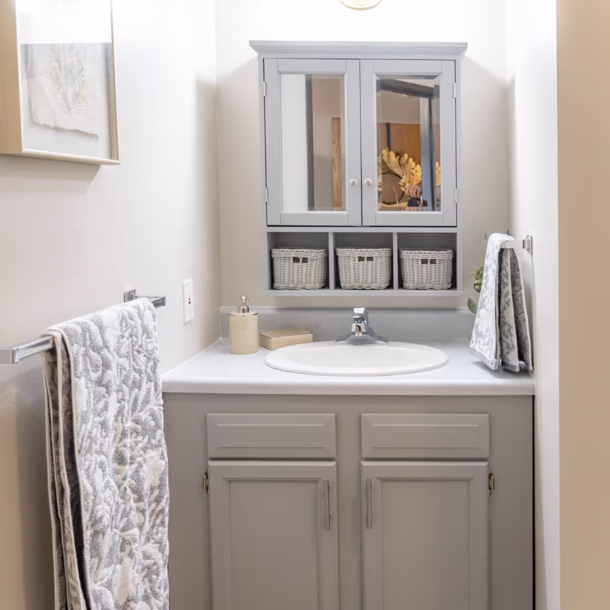 Bathroom vanity with gray cabinets, an oval sink, a mirrored medicine cabinet, and hanging towels.