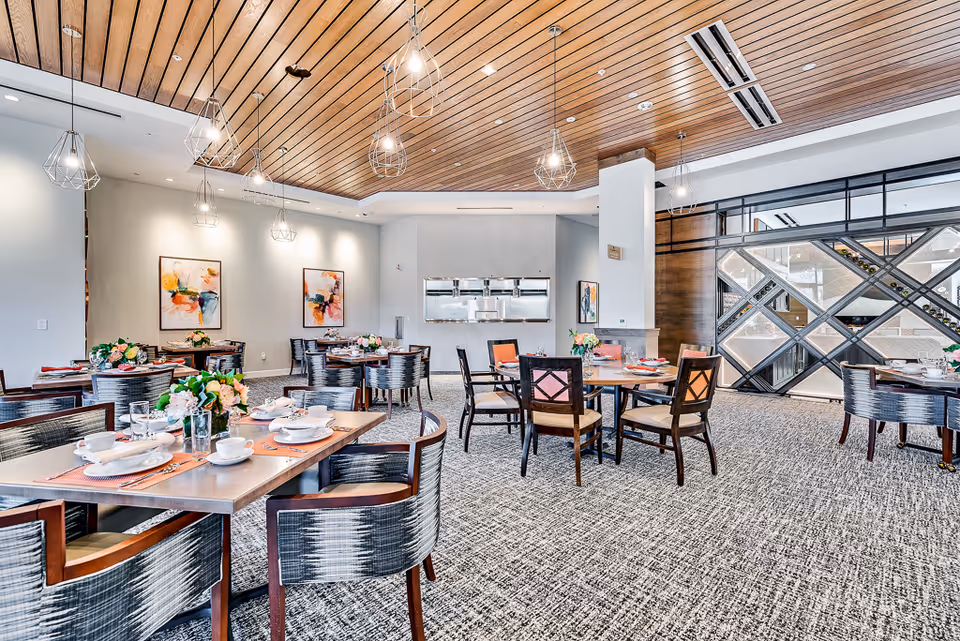 Bright contemporary dining room with multiple set tables, patterned chairs, pendant lights and wall artwork.