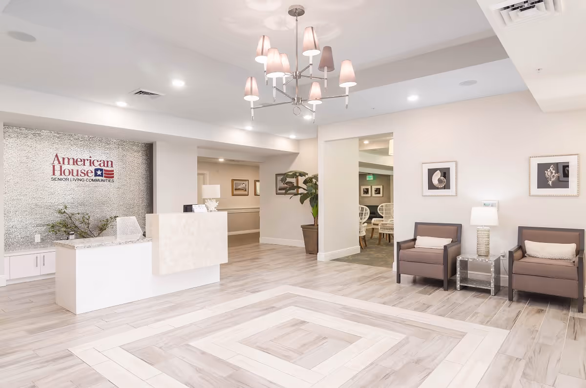 Bright reception lobby with a front desk, seating area, chandelier, and an 'American House' logo on the wall.