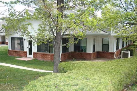 Exterior view of a single-story senior living facility with brick base and green landscaping.