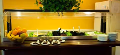 A self-serve buffet with fruit, desserts, and salad behind a glass sneeze guard.