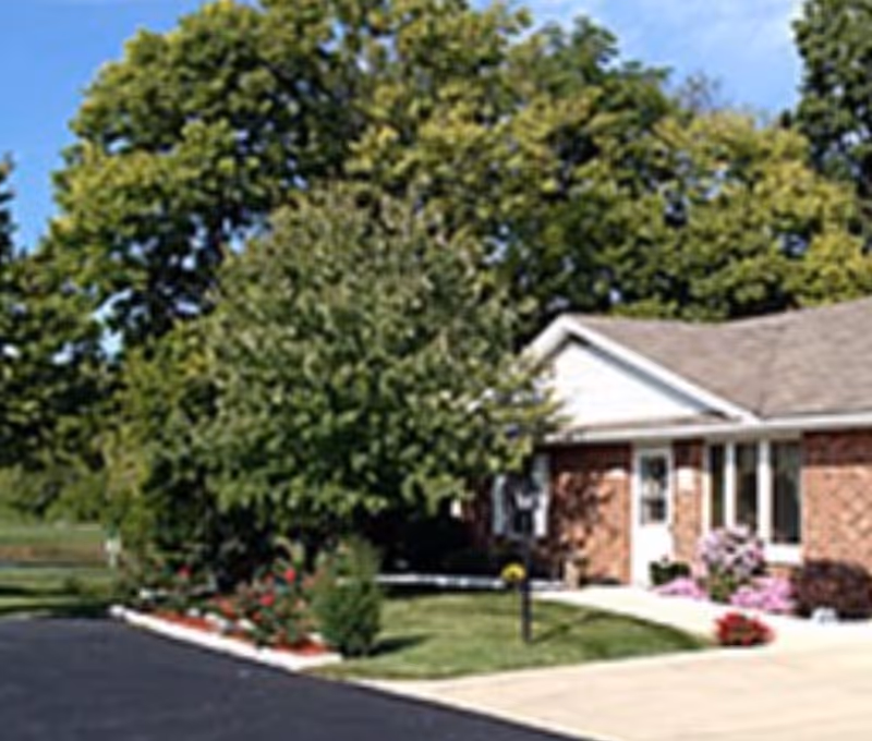 Front exterior of a single-story brick building with a large tree, landscaped lawn, and driveway.