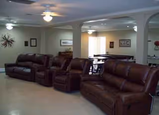 A spacious living room with brown leather couches and ceiling fans in a senior facility.
