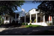 Front view of a white, single-story assisted living home with a porch and greenery
