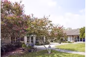 Front exterior view of The Guest House facility with trees and a walkway.