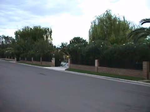 Exterior view of a gated residential entrance with hedges and brick fence.