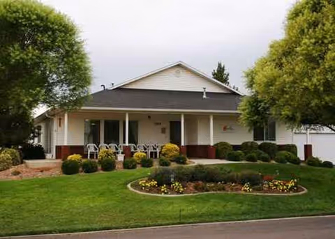 Exterior front of Beehive Homes of Kanab, showing chairs on the porch and a landscaped lawn.