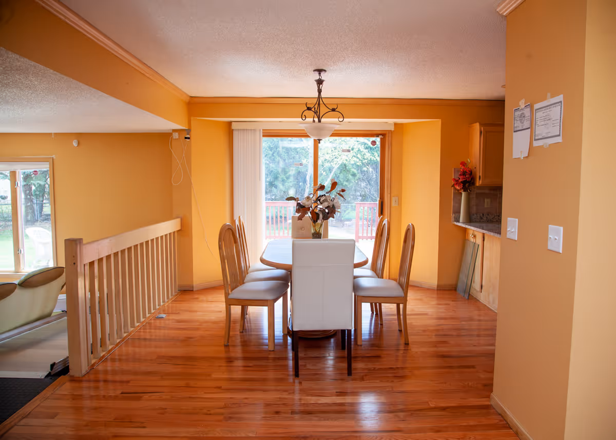 Dining area with a wooden table and six chairs on hardwood floors, warm yellow walls, a chandelier, and sliding glass doors to a deck.