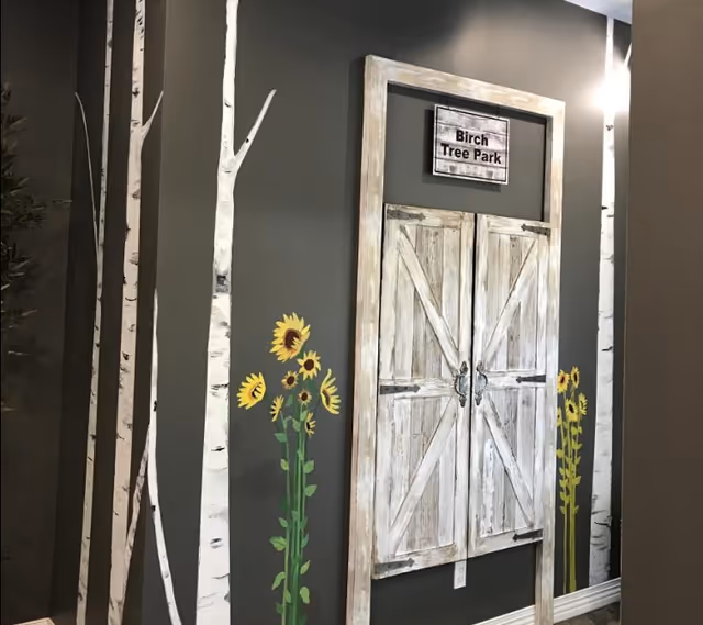 Decorative interior wall featuring rustic barn-style doors, birch tree decals, painted sunflowers and a 'Birch Tree Park' sign.