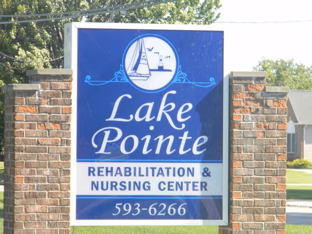 A blue and white roadside sign reading "Lake Pointe Rehabilitation & Nursing Center" mounted between brick pillars.