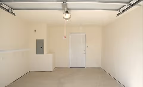 Empty single-car garage with a concrete floor, white walls, overhead garage door opener, and a side entry door.
