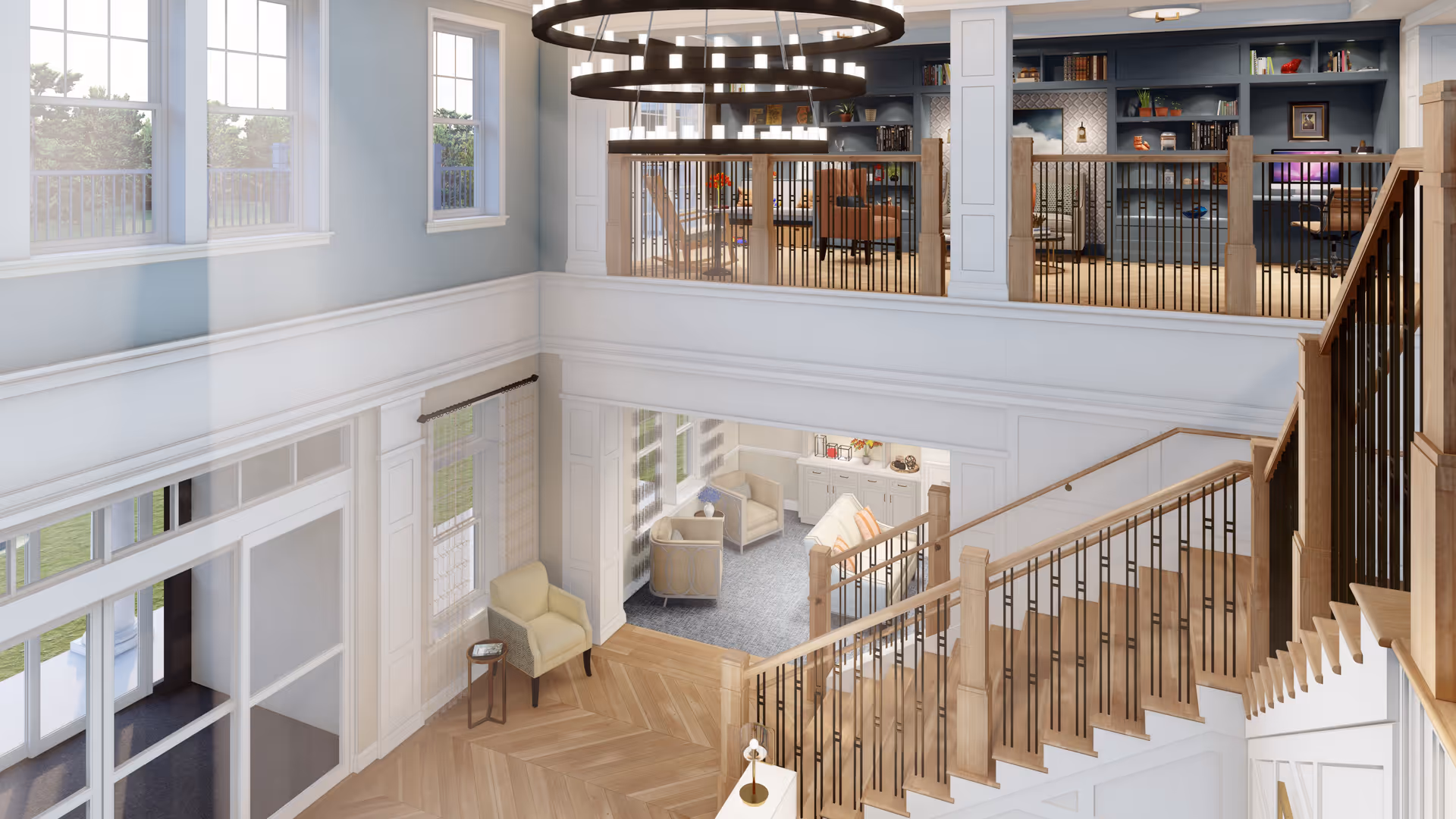 Interior view of a senior living facility featuring a spacious two-story common area with large windows, a wooden staircase with black metal railings, a seating area with armchairs and a small table, and a second-floor balcony with bookshelves and additional seating. The space is well-lit with natural light and modern circular chandeliers.