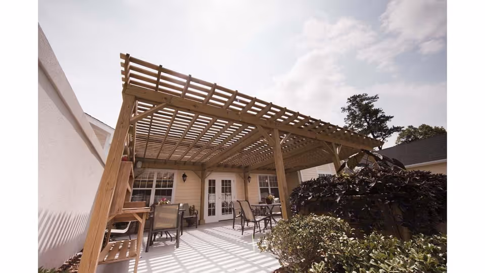 Wooden pergola-covered patio with outdoor seating and plants in front of a building's French doors.