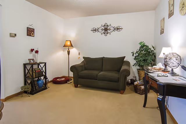 Cozy living room with a dark green loveseat centered against a white wall, a floor lamp, side table, and decorative accents.