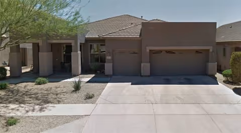 Single-story beige building with a three-bay garage and desert landscaping.