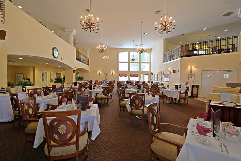 Spacious elegant dining room with multiple set tables, chandeliers, and a second-floor balcony.