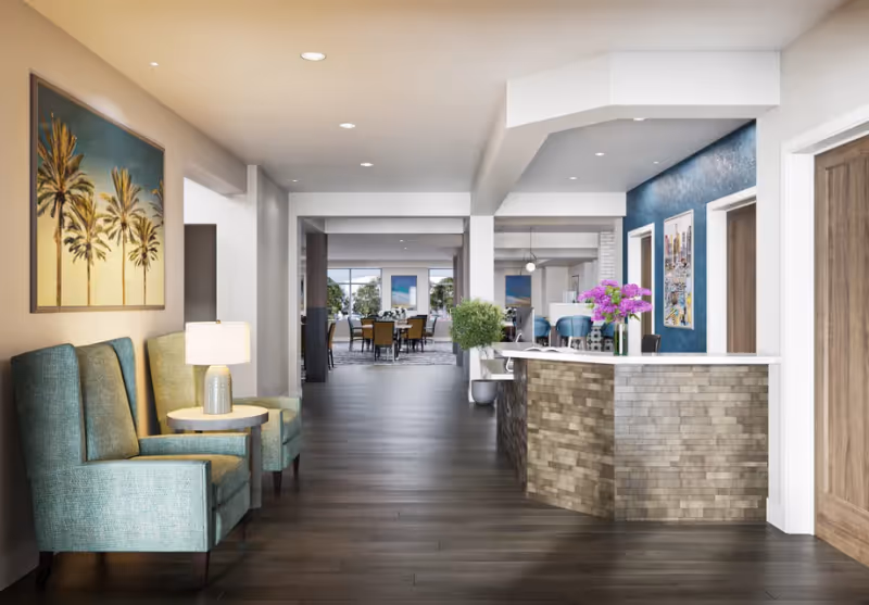 Bright interior reception and lounge area with teal armchairs, a curved front desk, and a dining area visible down the hallway.