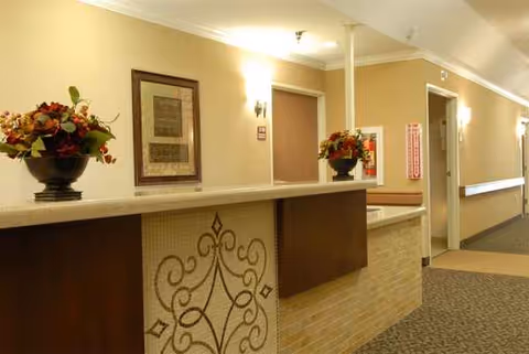 Beige hallway with a long reception desk, floral arrangements, and wall sconces.