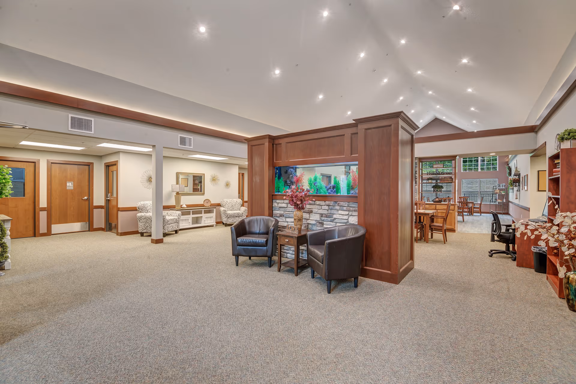 Spacious senior living common area with seating, an aquarium divider, and dining tables in the background.